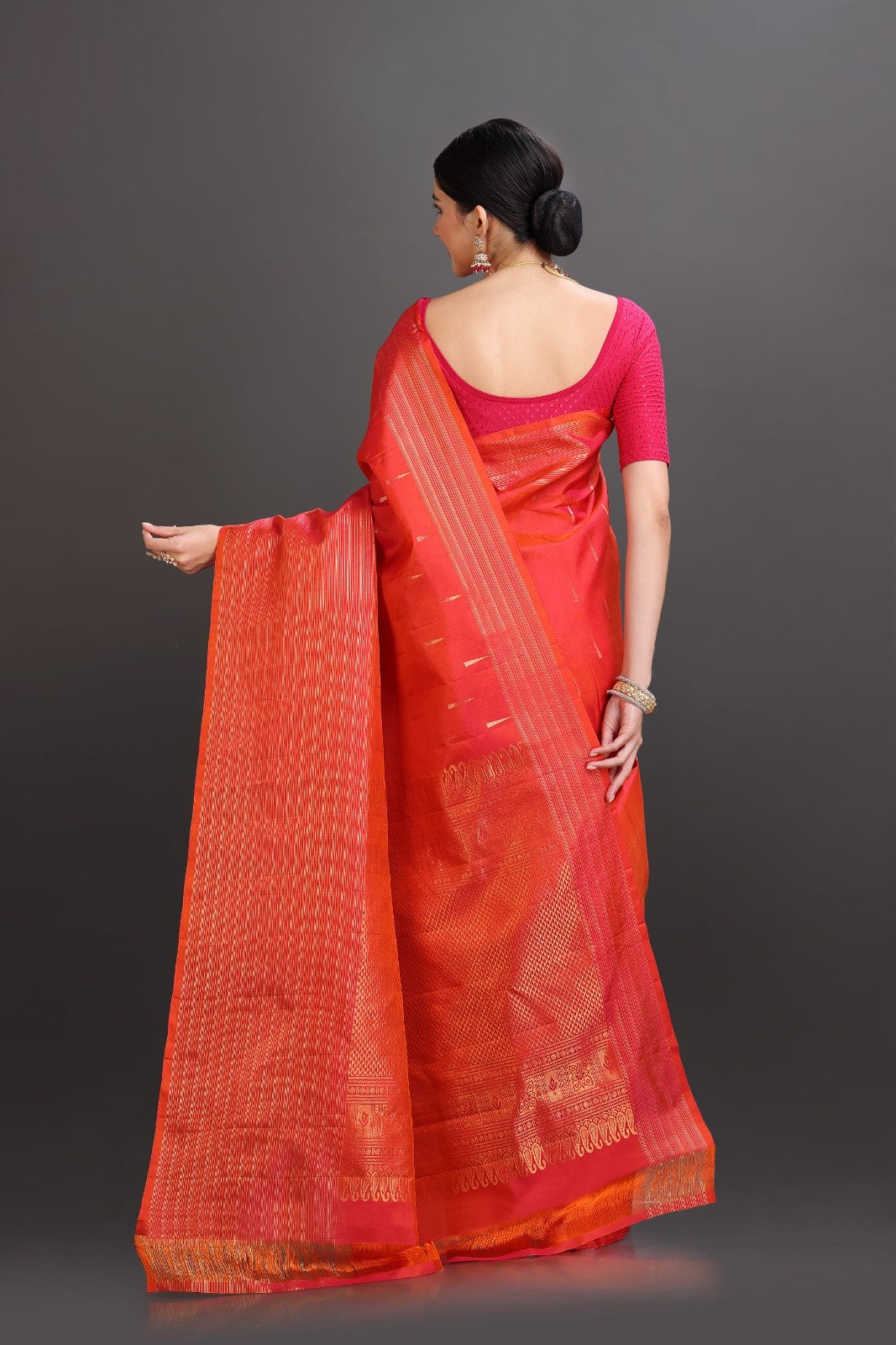 Woman wearing a red saree with a pink blouse against a gray background