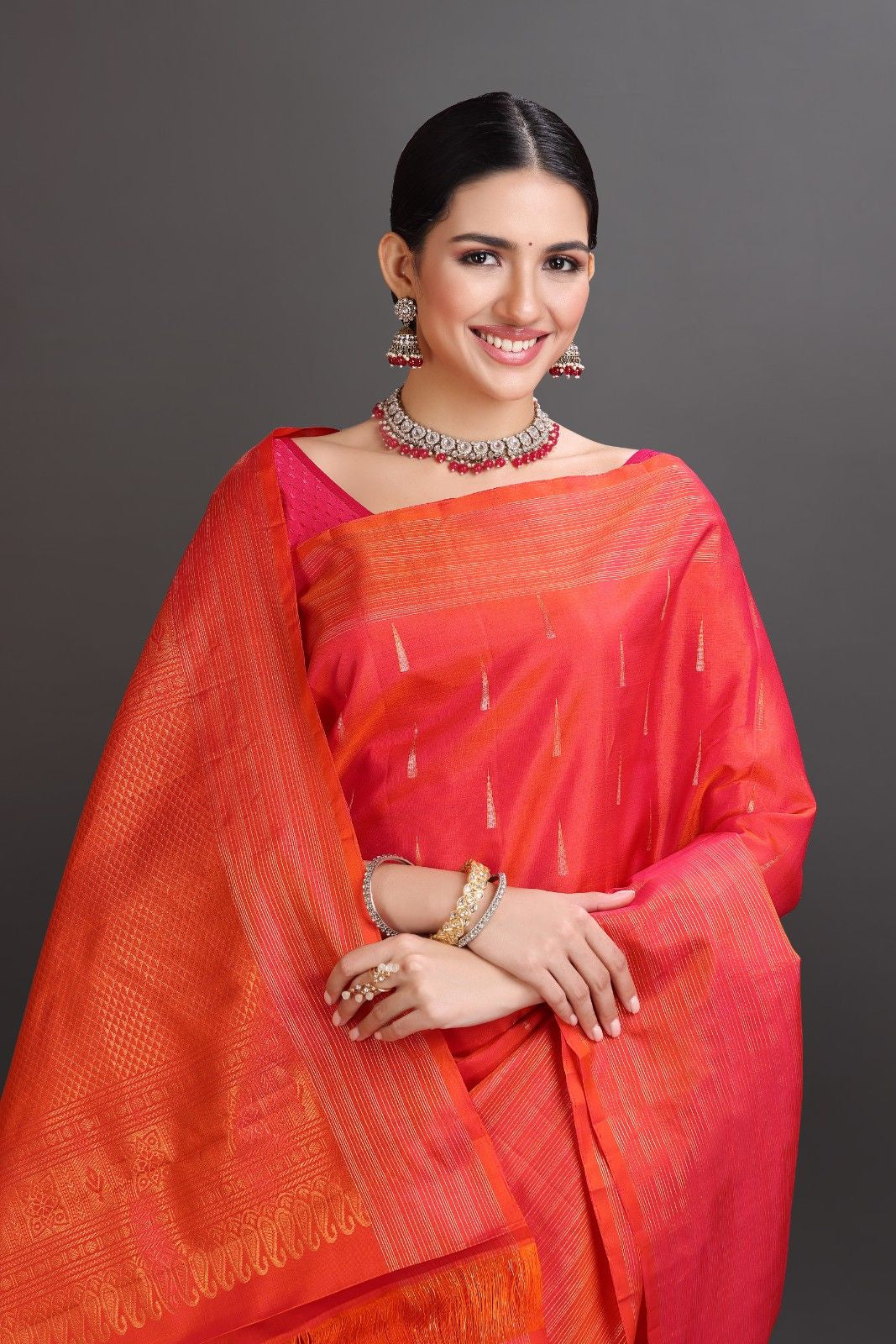 Woman wearing a bright orange saree with a gray background