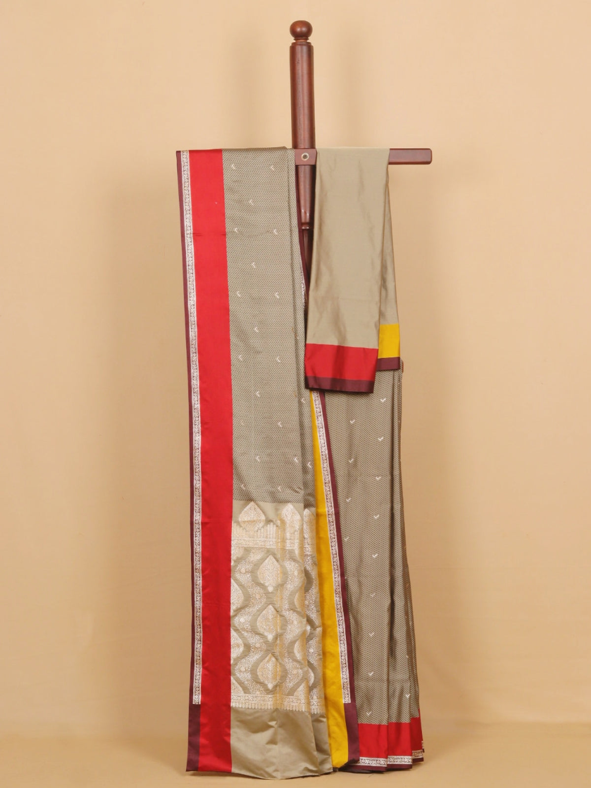 A draped gray saree with red, yellow, and white borders, displayed on a wooden hanger against a beige background.