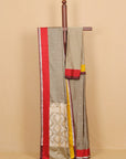 A draped gray saree with red, yellow, and white borders, displayed on a wooden hanger against a beige background.